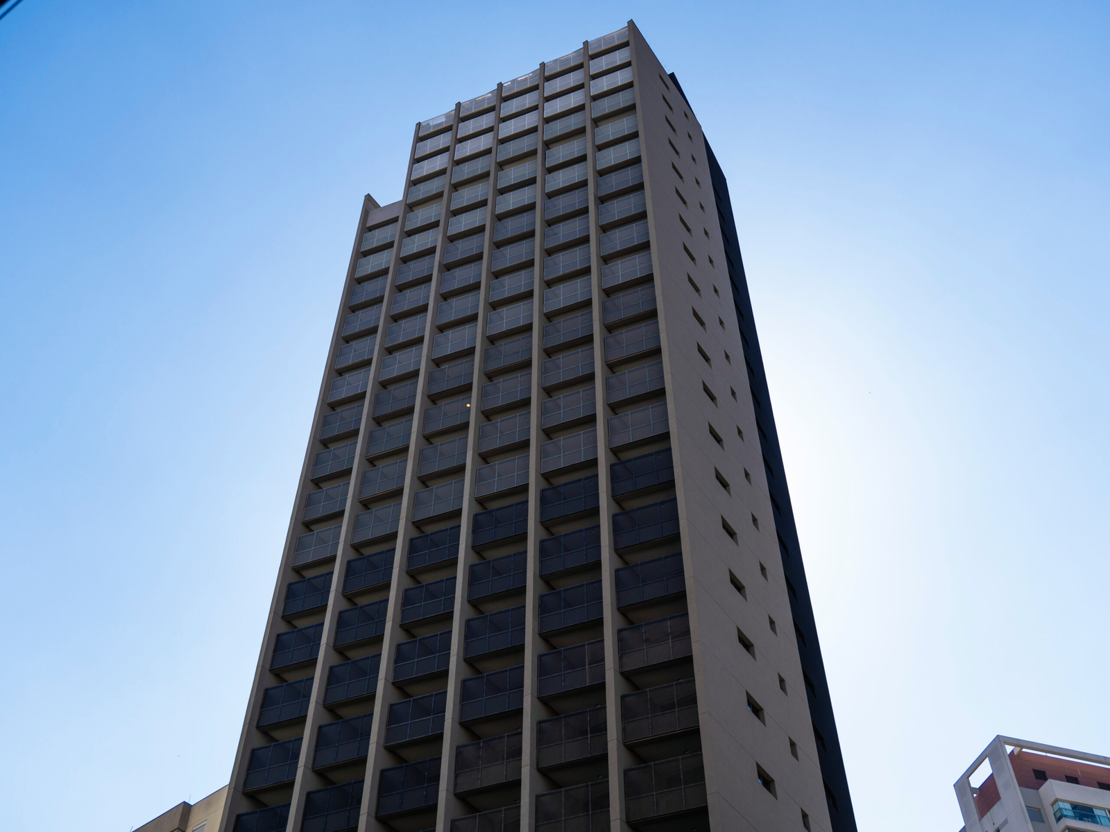 Fachada imponente do edifício On Vila Madalena com design moderno e céu azul límpido.