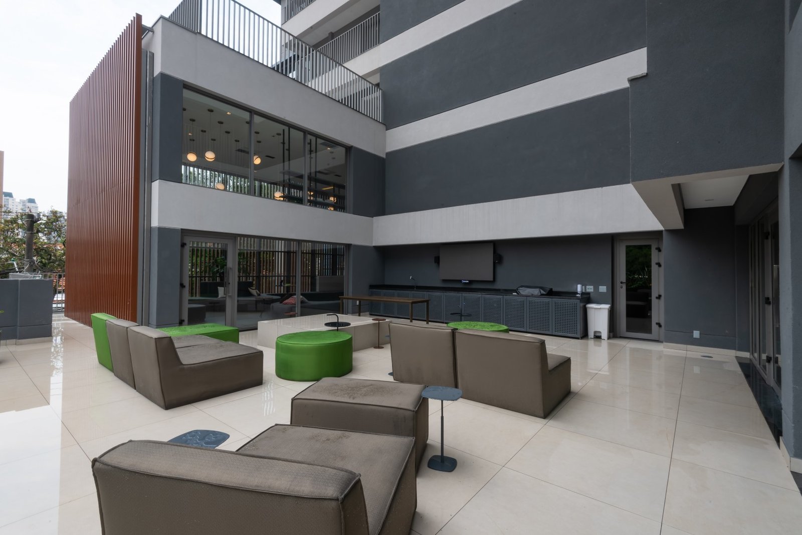 Vista ampla da fachada interna do prédio voltada para o terraço de convivência, ressaltando o acabamento moderno da arquitetura e as áreas de lazer externas.